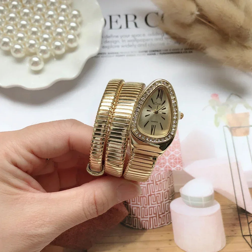 Gold bracelet with clock face held by a hand on a decorative surface with pearls and flowers.