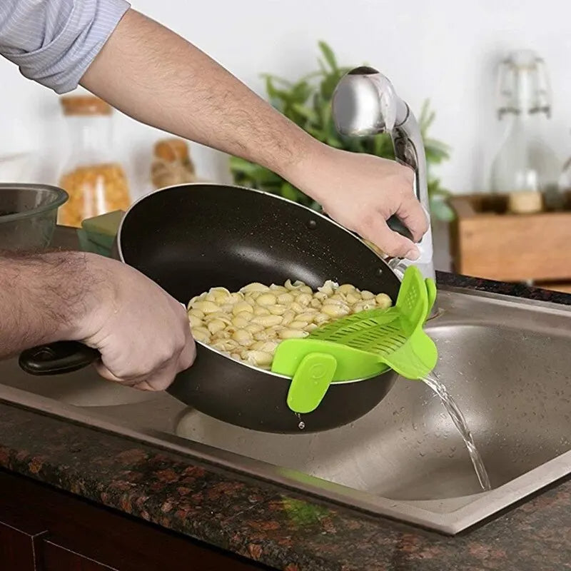 Person pouring pasta from a pan into a sink using a green kitchen tool.