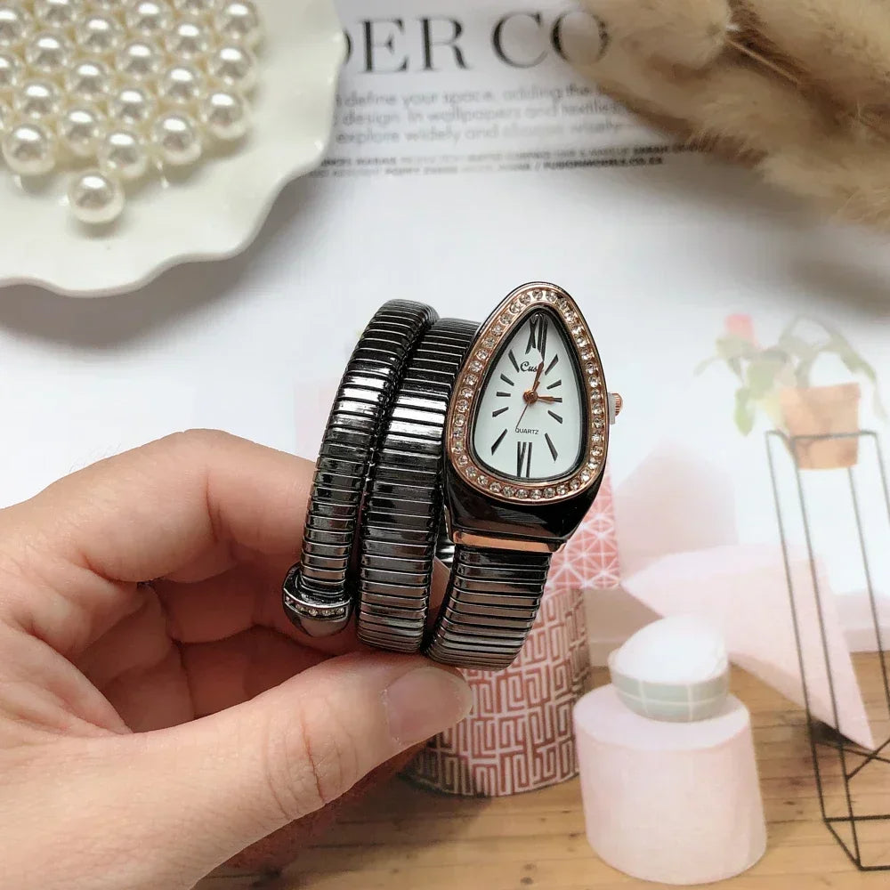 Hand holding a bracelet with a watch face, pearl necklace, and decorative items in the background.