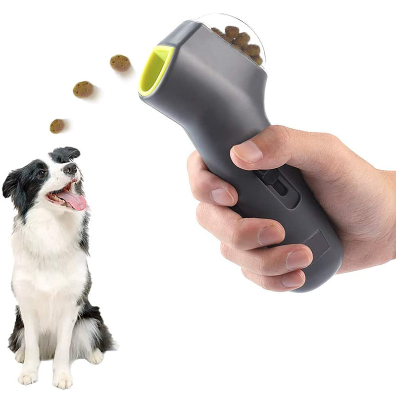 Hand holding a gray and green pet treat launcher device with a dog sitting next to it on a white background