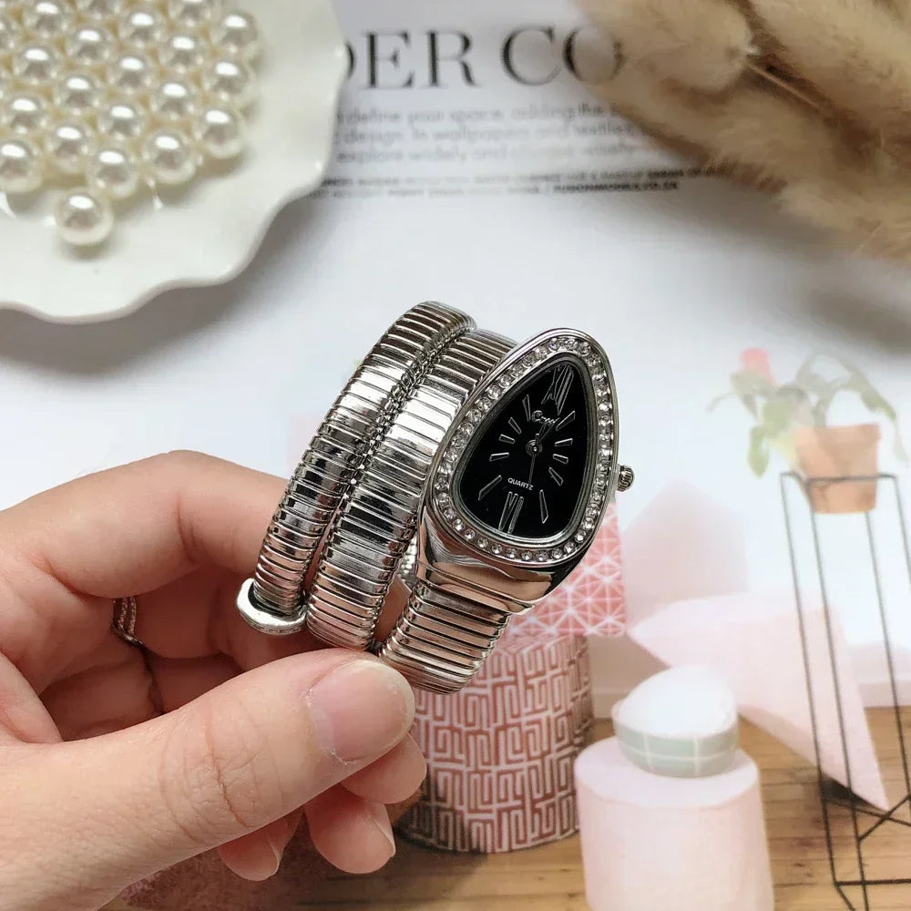 Silver watch with black face held by a hand on a blurred background