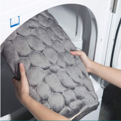 Person holding a textured gray mat in front of a washing machine