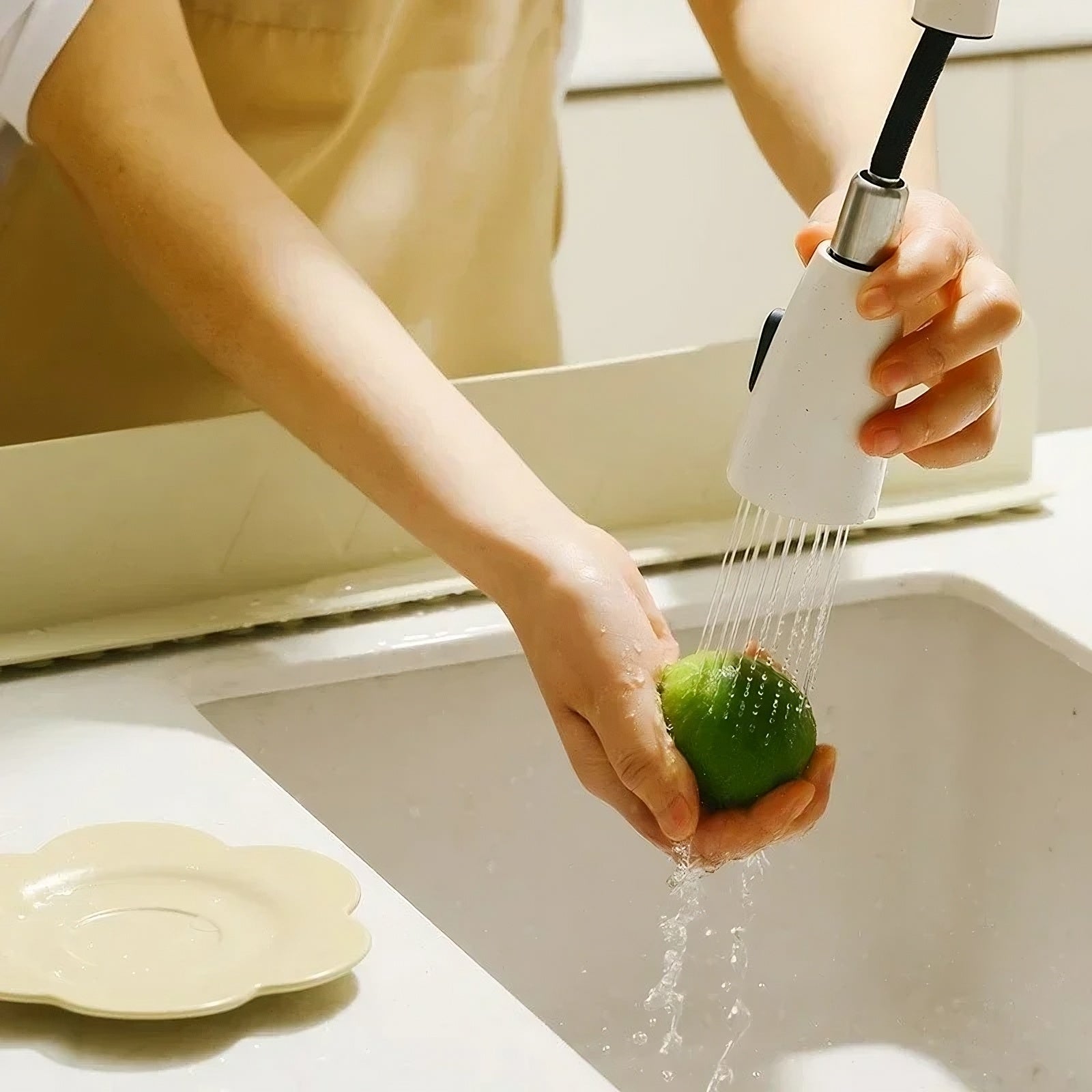 Person washing a green apple under a faucet in a kitchen sink protected by a splash guard